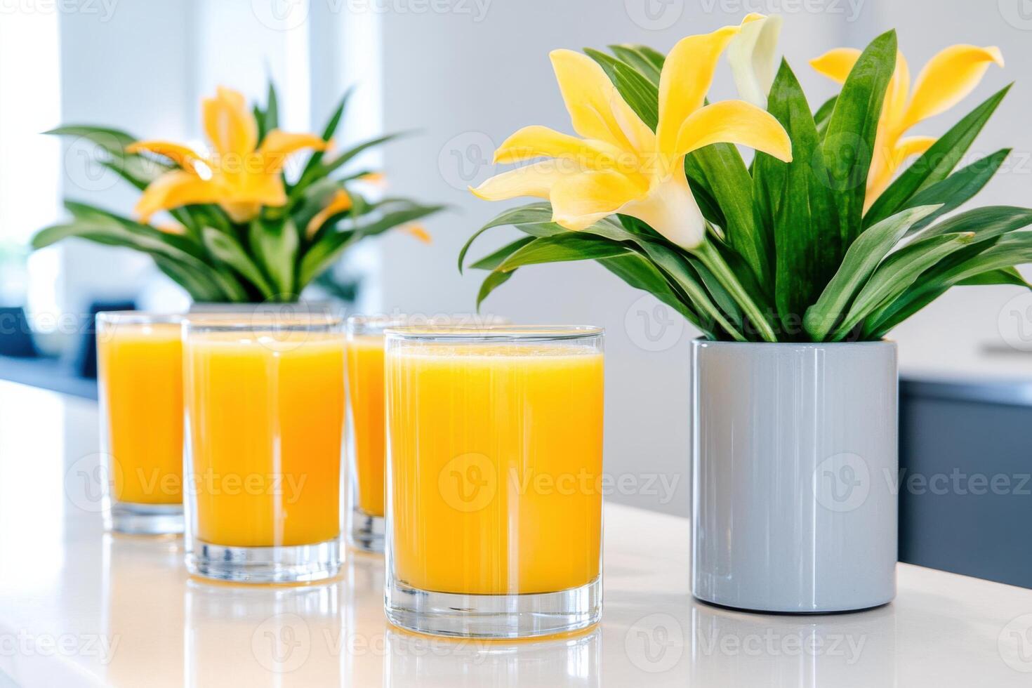 Fresh juice bar with vibrant golden-yellow juices and decorative floral arrangements on a sleek gray counter in a modern setting photo