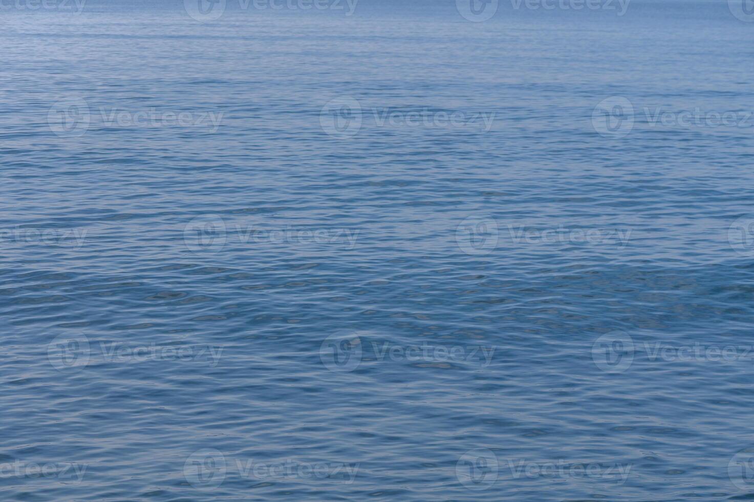 Calm waves gently lap against the shore at a tranquil seaside location in midday sunlight photo