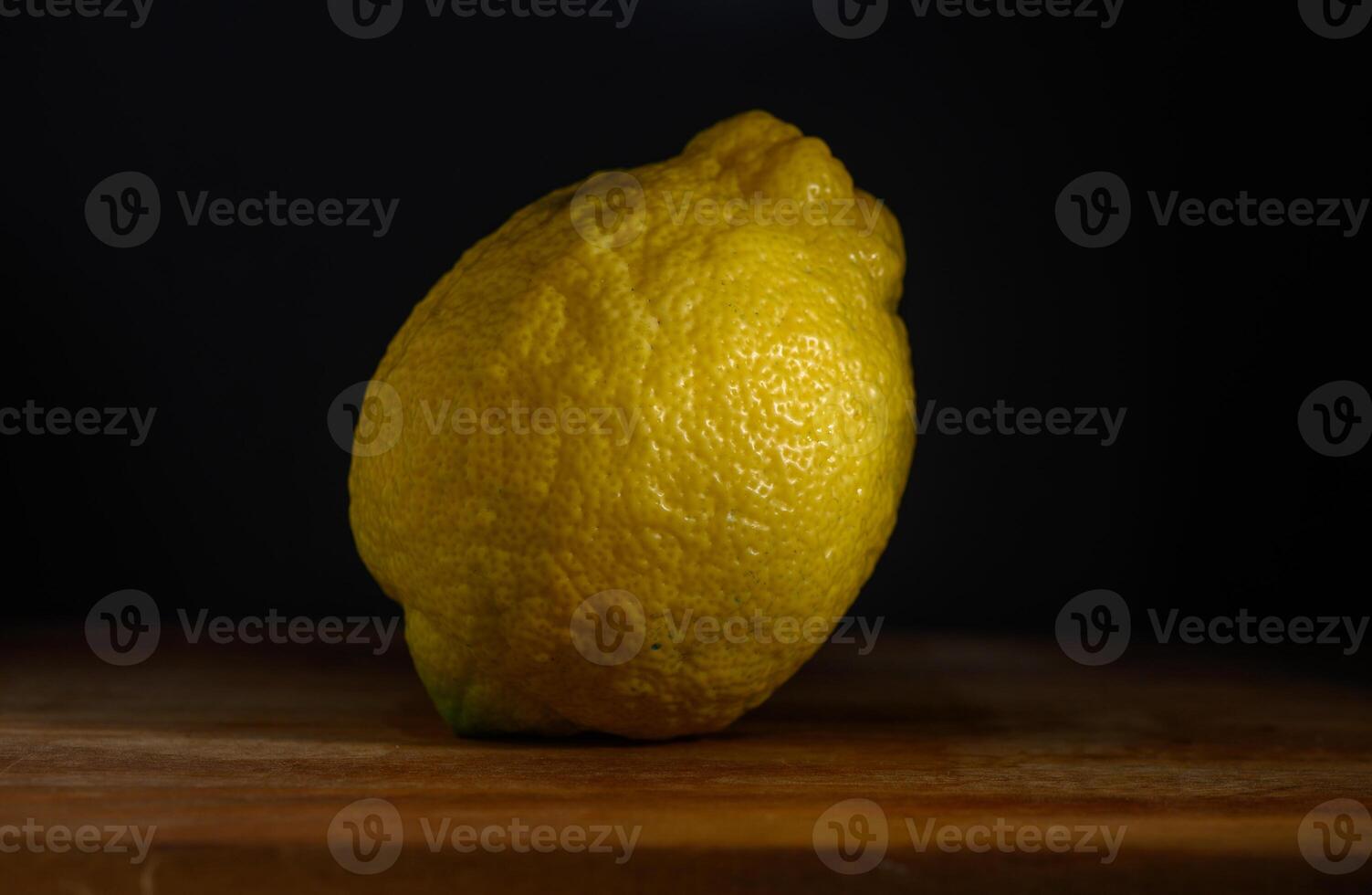Bright yellow lemon resting on a wooden surface with soft shadows in the background under warm lighting photo