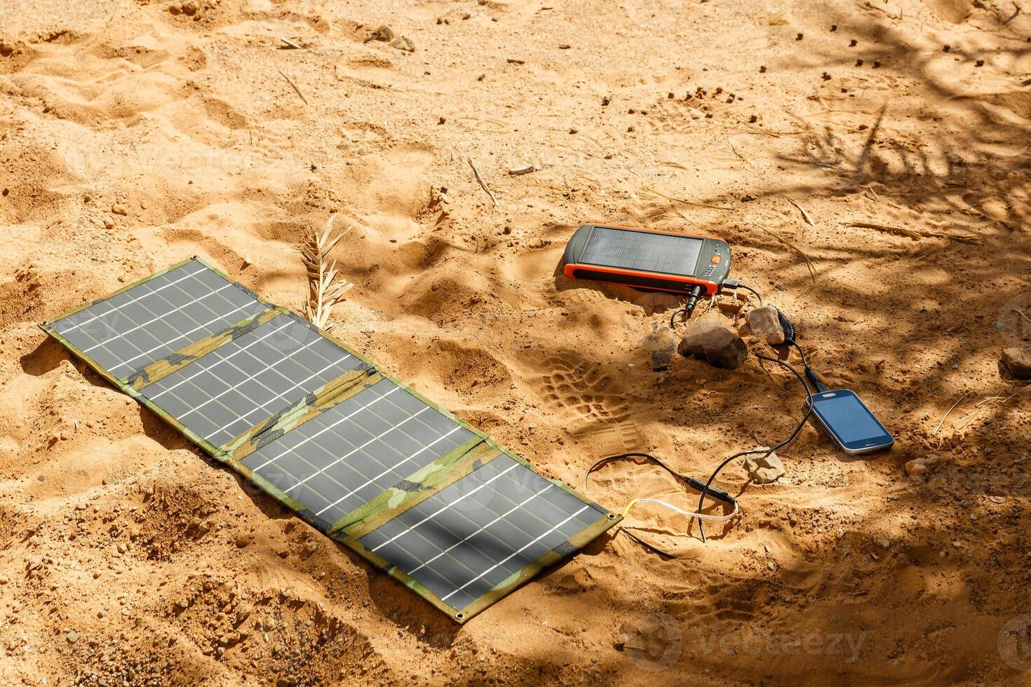 solar panel lying on the ground and charges the smart phone, the Sahara desert. Charge smart phone from the solar battery. photo