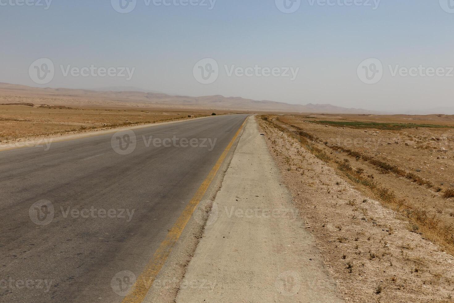 Road stretches across arid landscape in Kunduz Province, Afghanistan under clear skies photo