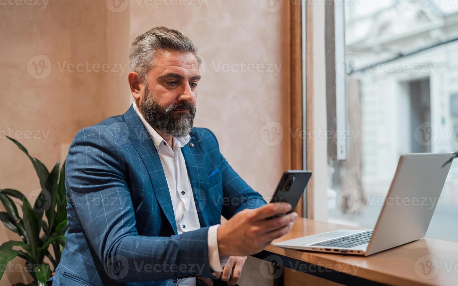A happy mature business man using his phone while working on a laptop in the office or cafe restaurant. photo
