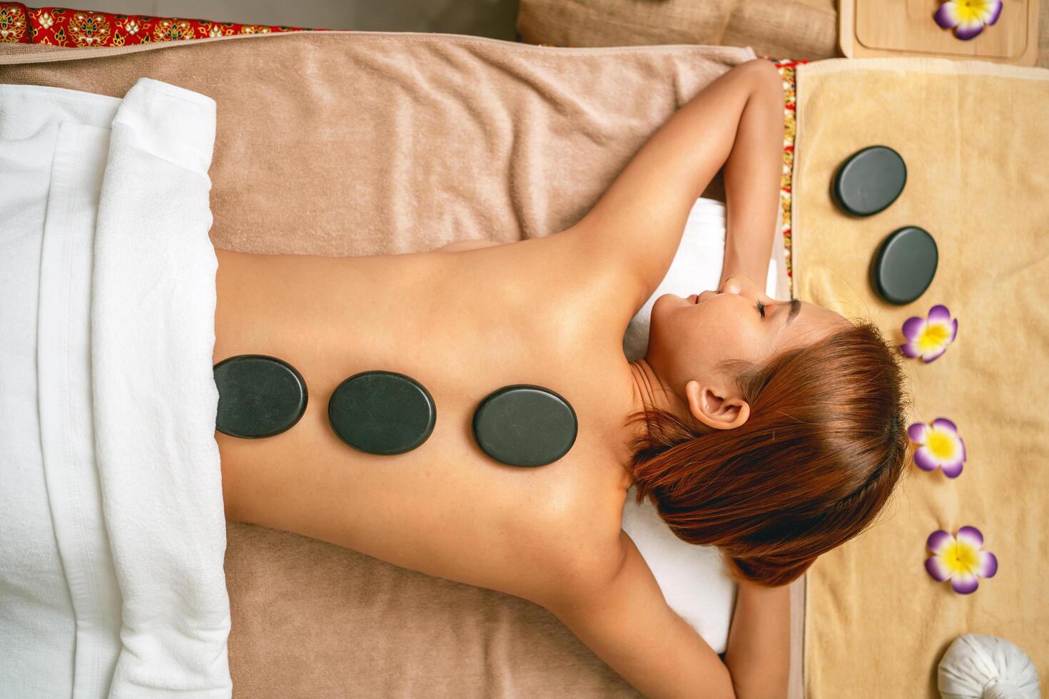 woman is laying on a massage table with four black stones on her back photo