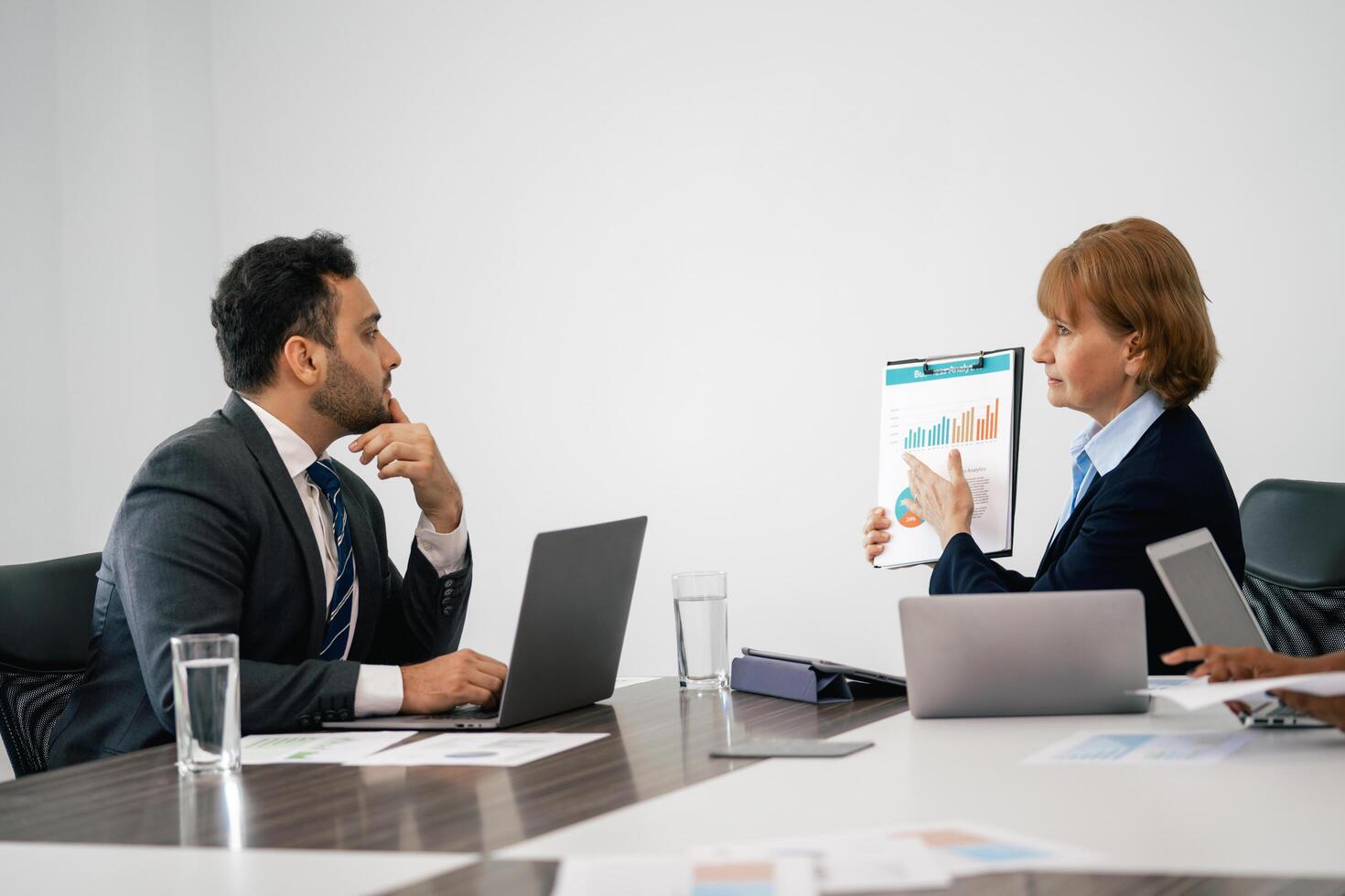 Two people in suits are sitting at a table with a presentation in front of them photo