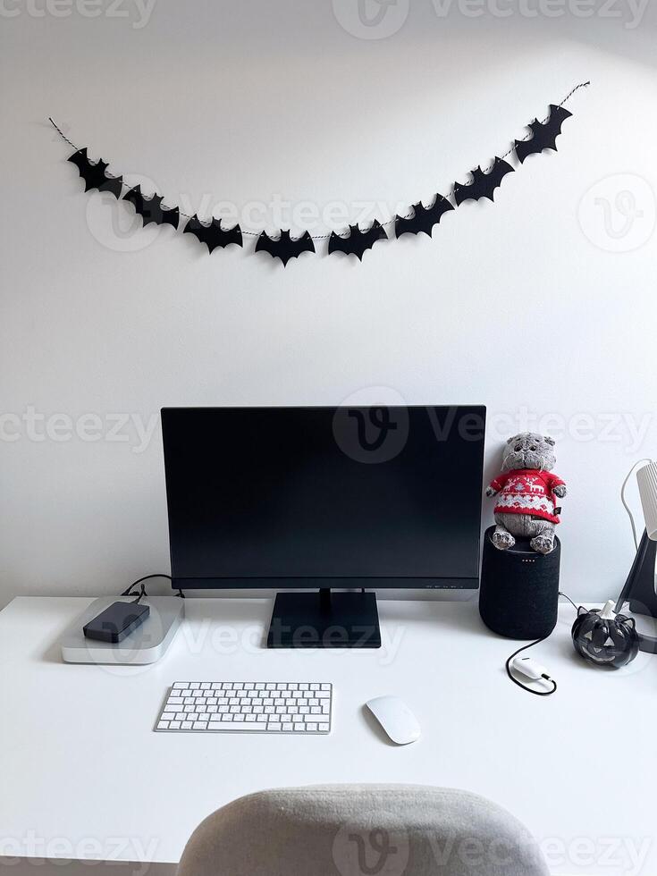 Clean and minimalistic home office desk decorated with halloween inspired black bat garland. Workspace combines functionality and seasonal charm, reflecting a balance of productivity and festivity photo