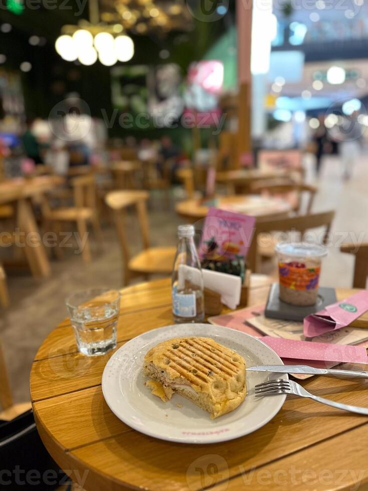 Freshly grilled sandwich rests on a white plate, surrounded by a casual dining ambiance. Natural light highlights the textures of bread and filling, creating a simple yet appetizing moment photo
