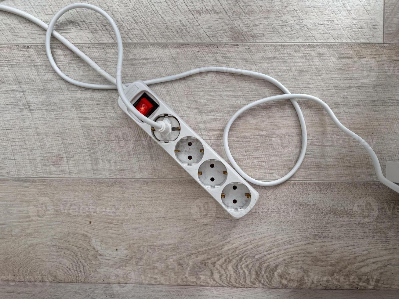 An extension cord with multiple outlets lying on a wooden floor. Practicality and utility in modern home setups. Electric power concept photo
