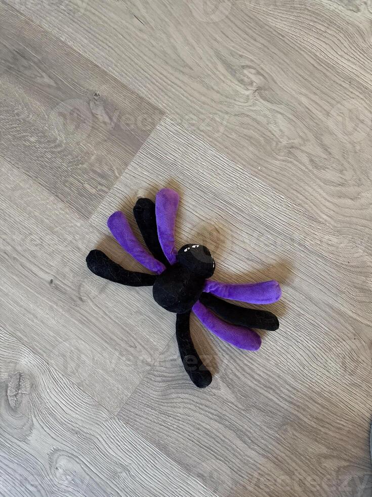 Plush spider toy with purple and black legs rests on a light wooden floor, creating a whimsical and playful atmosphere. Fun and creativity in everyday life photo