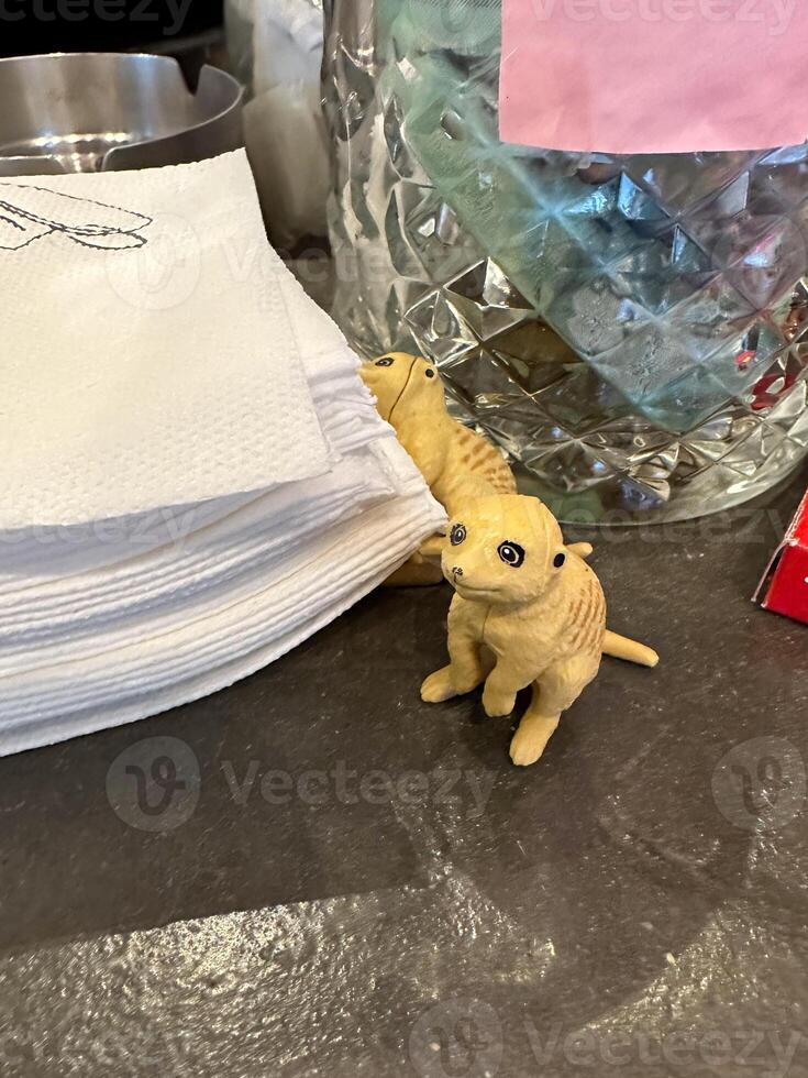 Small meerkat figurines sitting beside folded napkins on a cafe counter. A charming detail adds personality to a casual coffee shop setting photo