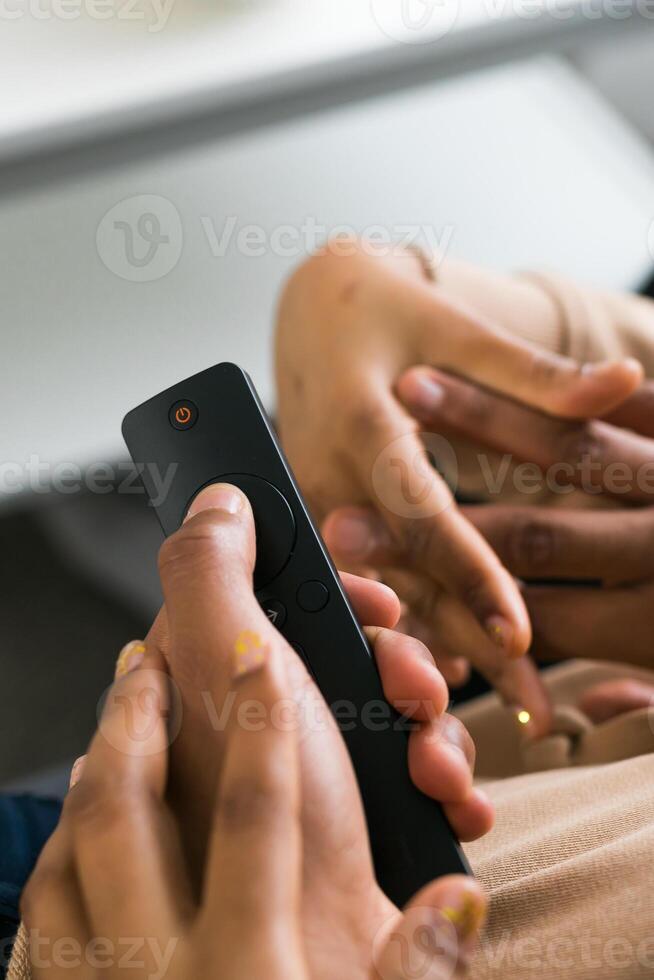 Hand holds a remote control while a bowl of popcorn sits on a white table in a modern living room. Relaxing and cozy atmosphere, perfect for watching movies or streaming content at home photo