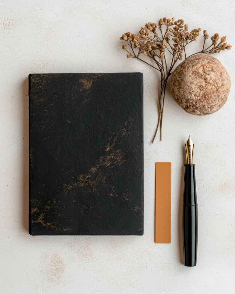 Flatlay of black notebook, fountain pen, dried flowers, and stone on white background photo