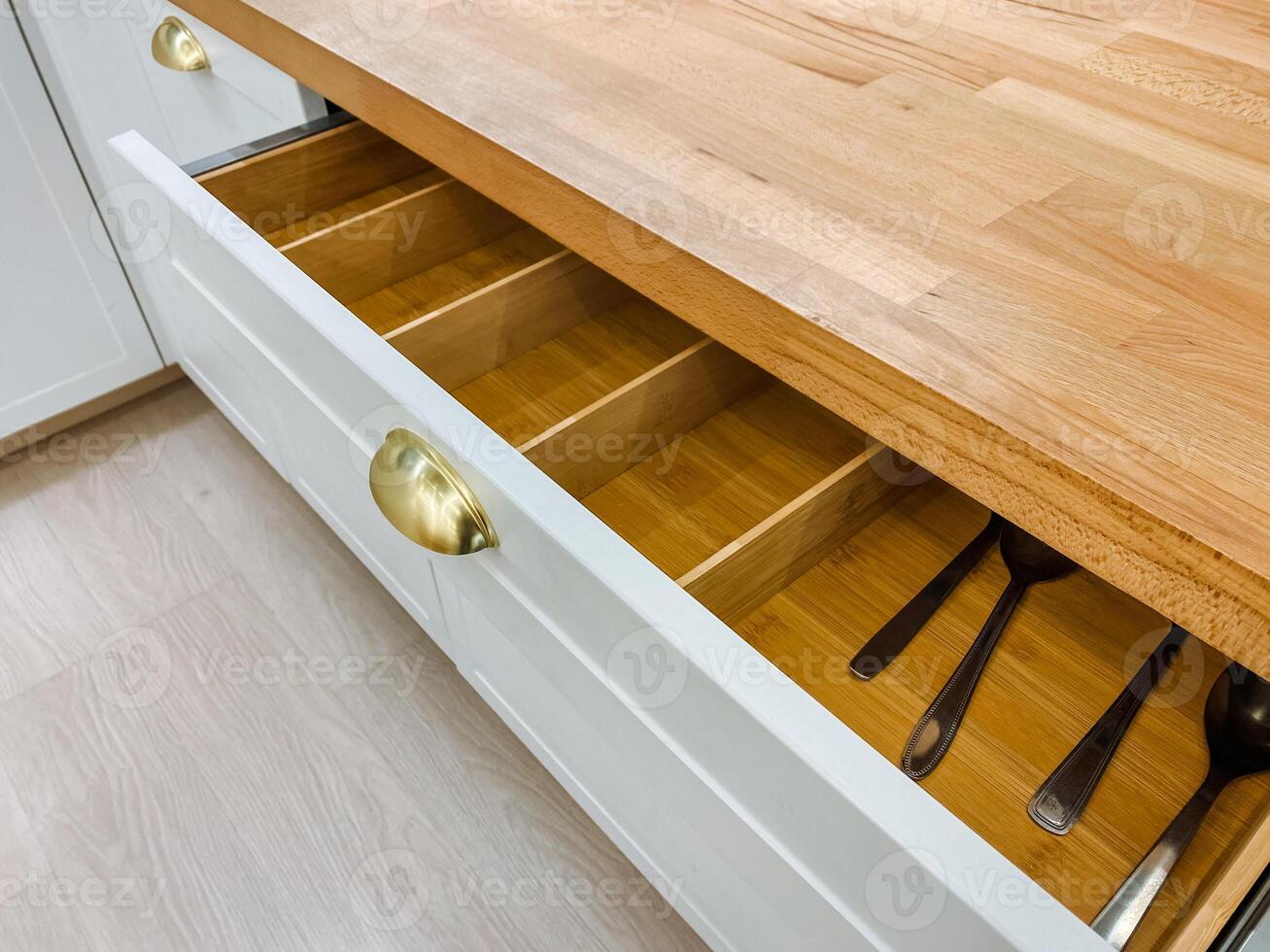 In the kitchen, there is a drawer loaded with various utensils, resting on a beautiful wooden counter top that enhances the overall aesthetic and functionality of the space photo