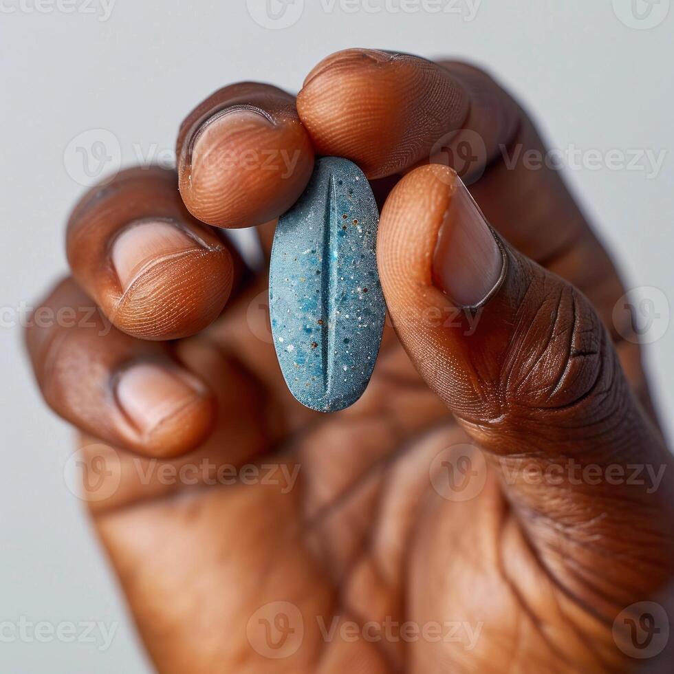A hand holds a blue capsule pill against a plain background photo