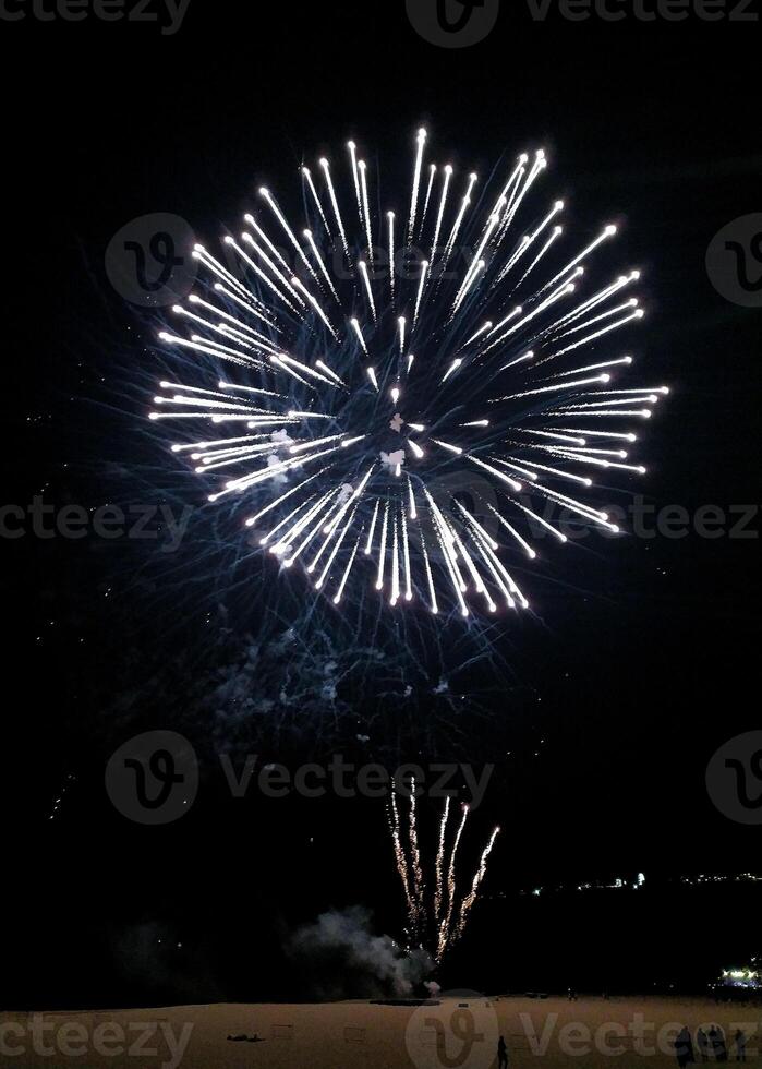 Stunning fireworks display illuminating the night sky above a beach. Bright, white bursts create a captivating spectacle perfect for celebratory themes, holiday promotions, or travel advertising. photo