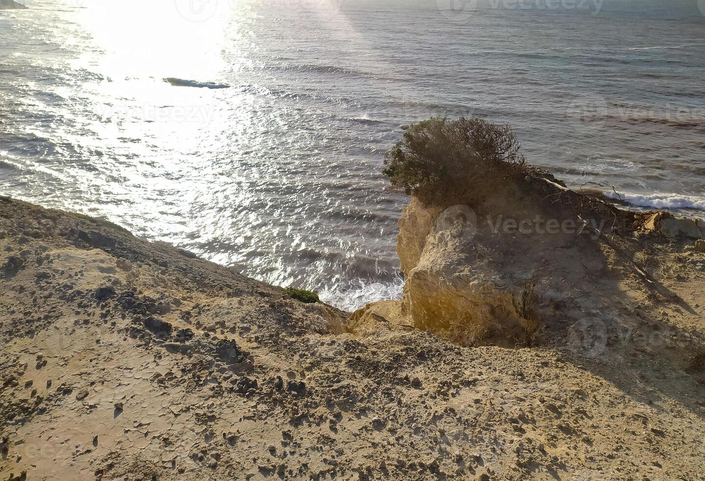 Coastal cliff view of rough waves against the rocks in the afternoon sunlight at a scenic seaside location photo
