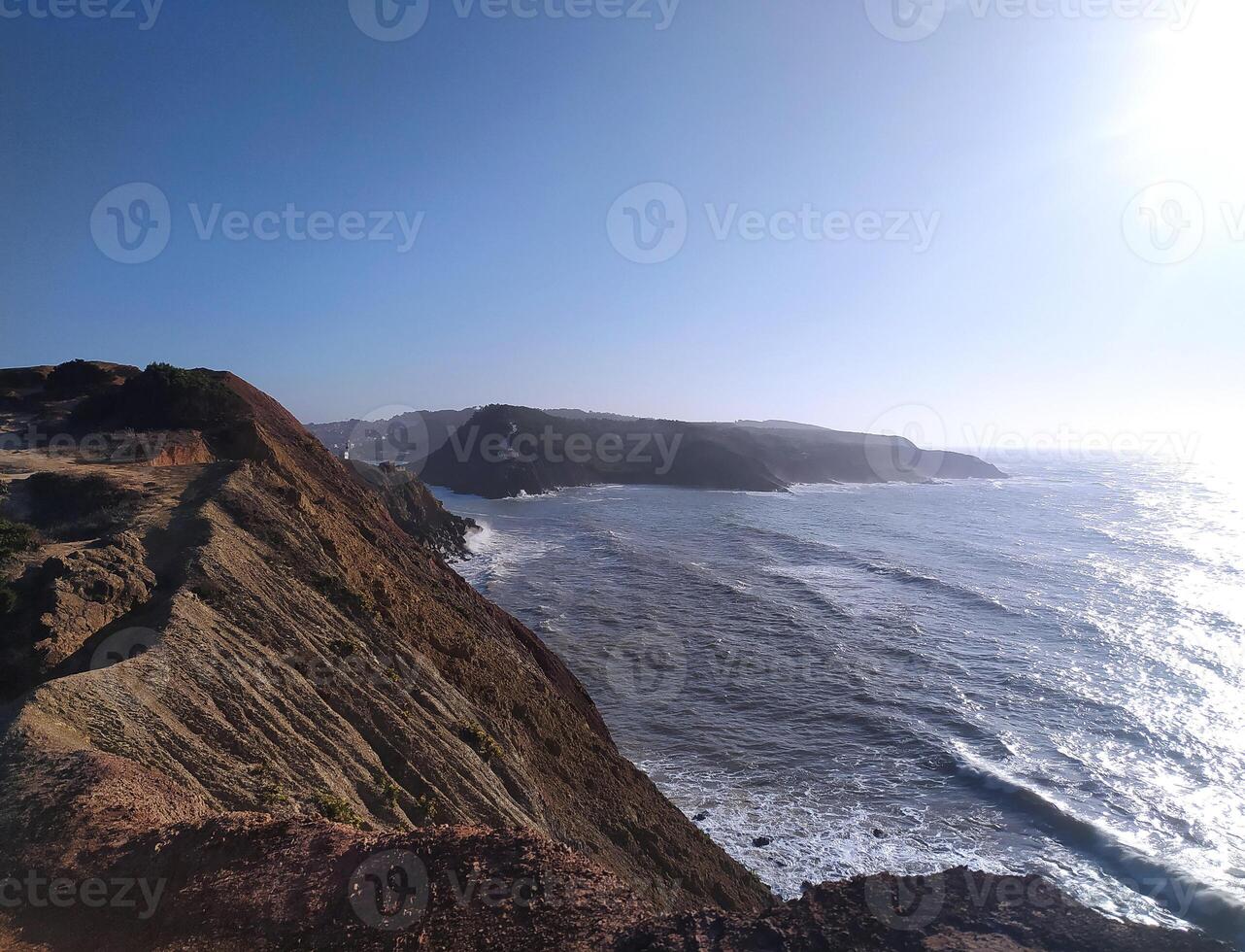 Coastal cliff view of waves against the rocks in the afternoon sunlight at a scenic seaside location photo