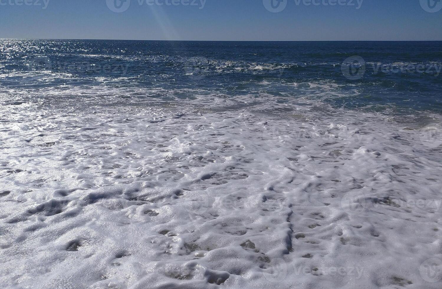 A serene beach at midday with gens lapping the shore and clear blue skies inviting relaxation photo