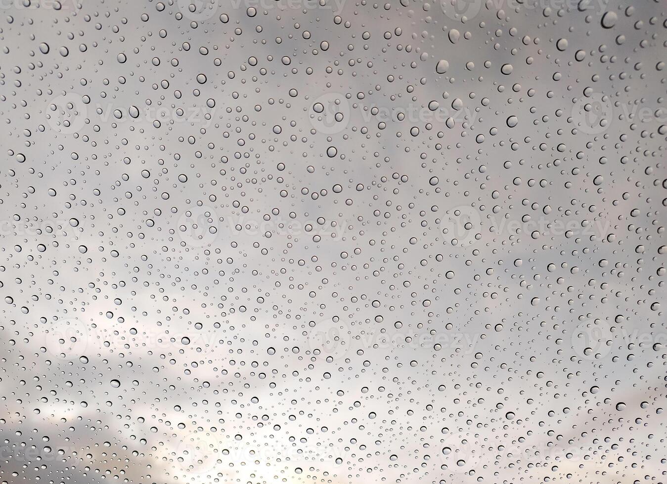 Stunning macro shot of water droplets on glass, showcasing a captivating texture against a blurred cloudy sky. Ideal for backgrounds, websites, or design projects needing a tranquil, atmospheric feel. photo