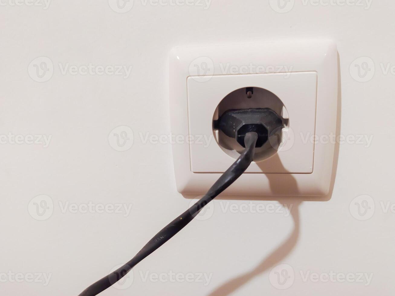 Closeup of a black power plugged into a white electrical outlet on a light wall. Simple, clean aesthetic perfect for illustrating electricity, power, or home appliance concepts. photo