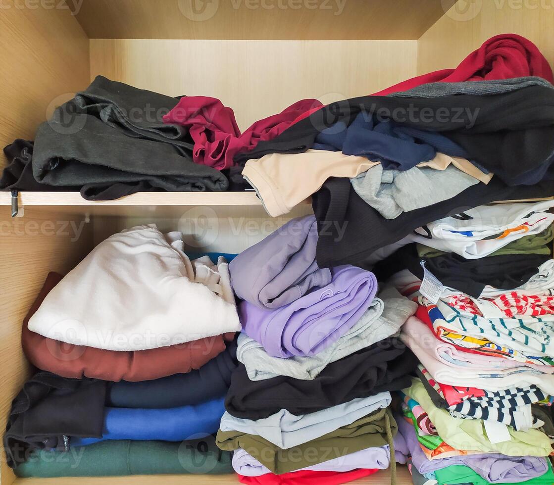 Neatly stacked and casually folded clothes fill a wooden wardrobe. photo