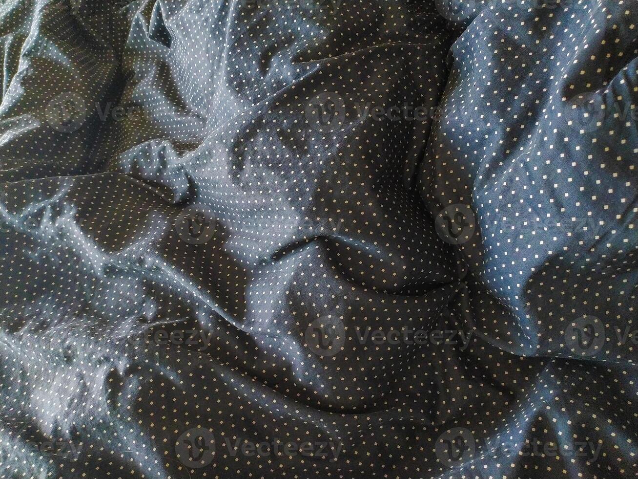 Closeup of textured dark fabric with a subtle polka dot pattern. The wrinkles and folds create a visually interesting surface ideal for backgrounds, website banners, or textile design projects. photo