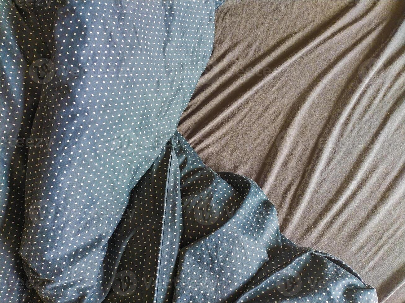 Closeup shot of a darkcolored bedsheet with a white polka dot pattern draped artfully over a solidcolored sheet. Perfect for illustrating concepts of sleep, rest, comfort, or textile design. photo