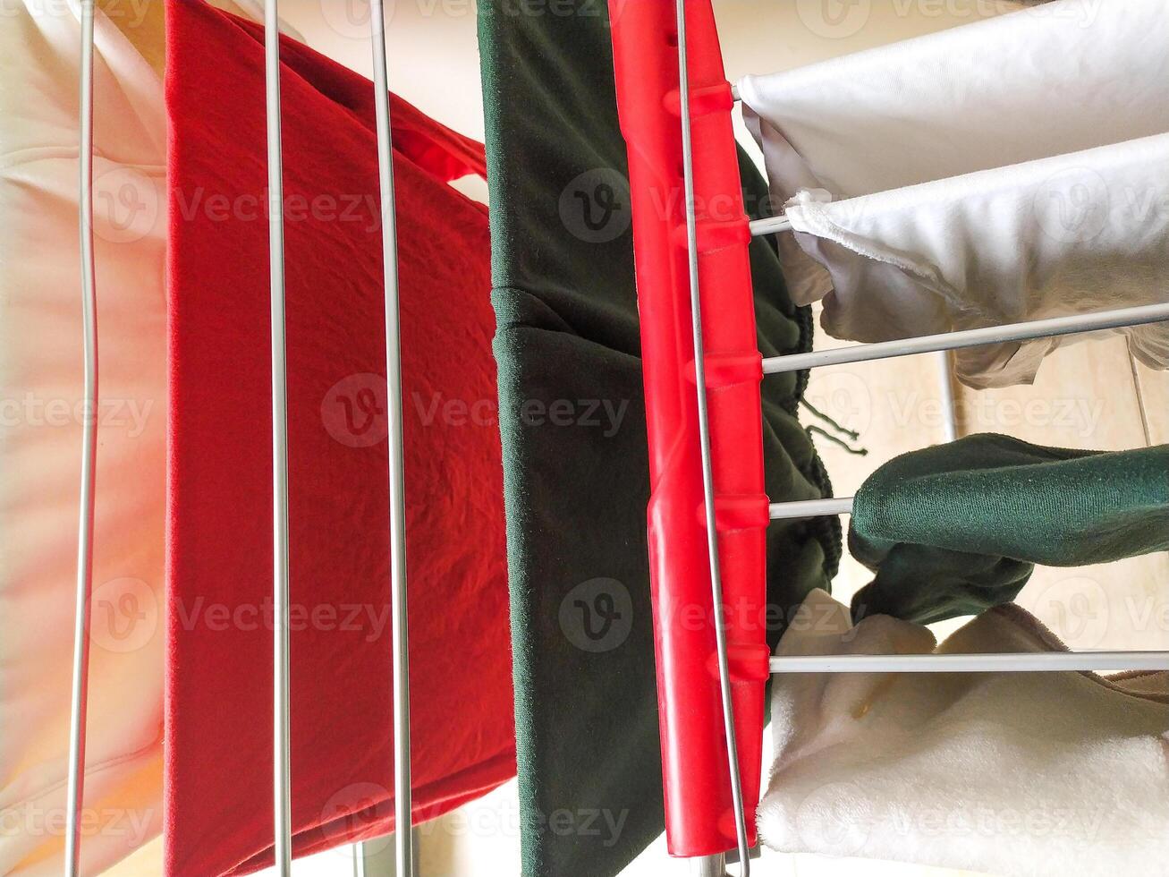Closeup view of freshly laundered clothing drying on a clothes rack. Red, white, and dark green garments hang neatly, showcasing vibrant colors and soft textures. photo