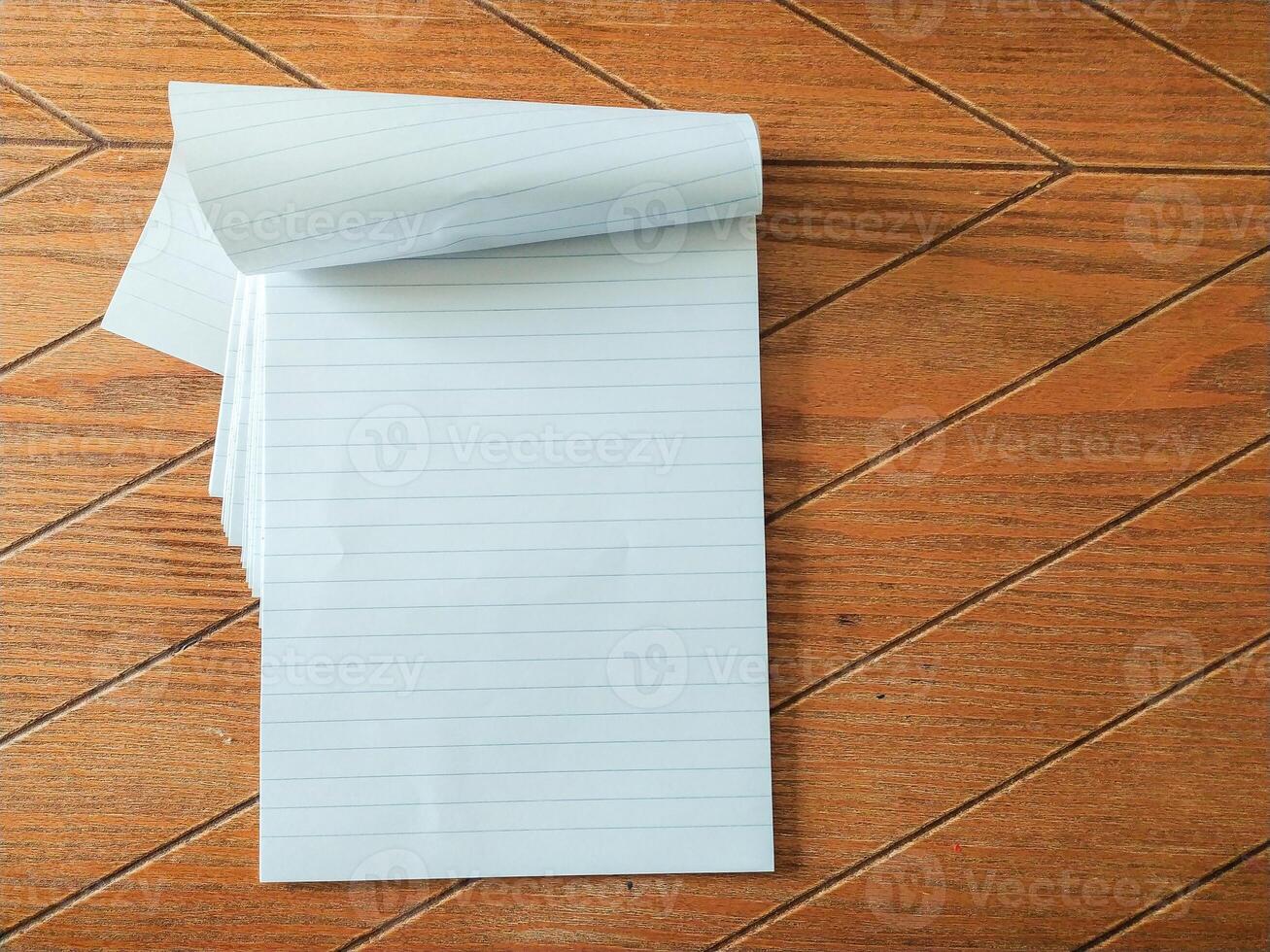 Blank lined notepad pages partially rolled, resting on a brown woodgrain surface. Perfect for showcasing your message, quotes, or product information. photo