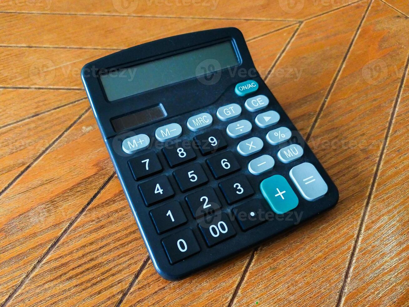 A slightly dusty, black calculator rests on a warm brown wood surface. Its simple design and clear display make it perfect for illustrating concepts of finance, math, or everyday calculations. photo