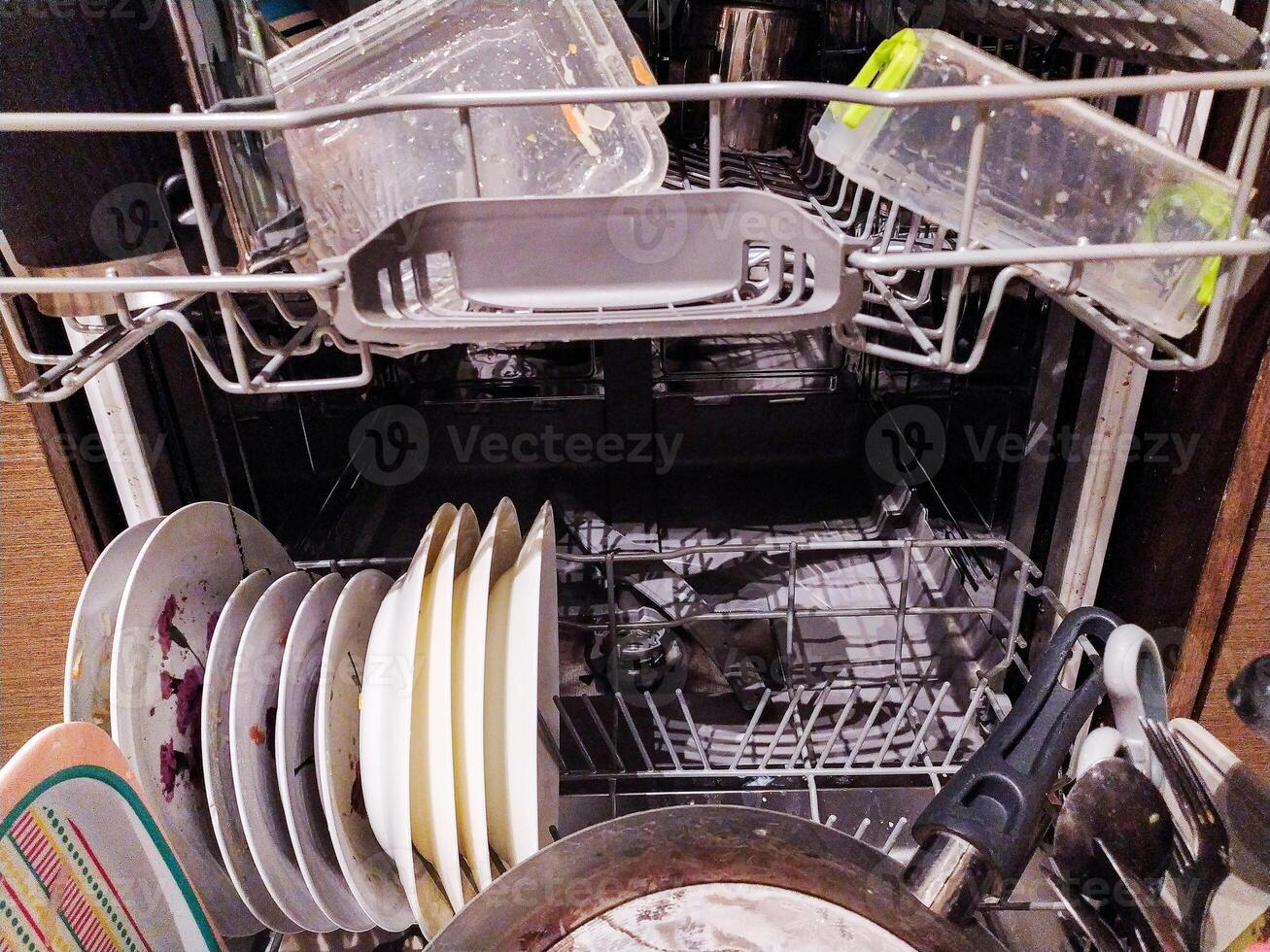 A messy, full dishwasher, overflowing with dirty dishes and food remnants. Ideal for illustrating the need for a powerful dishwasher or highlighting the challenges of cleaning up after a large meal. photo