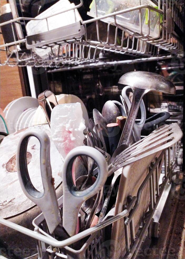 Closeup of silverware, kitchen utensils, and dishes in a dishwasher. The image showcases a realistic, slightly messy, yet appealing view of everyday kitchen life. photo