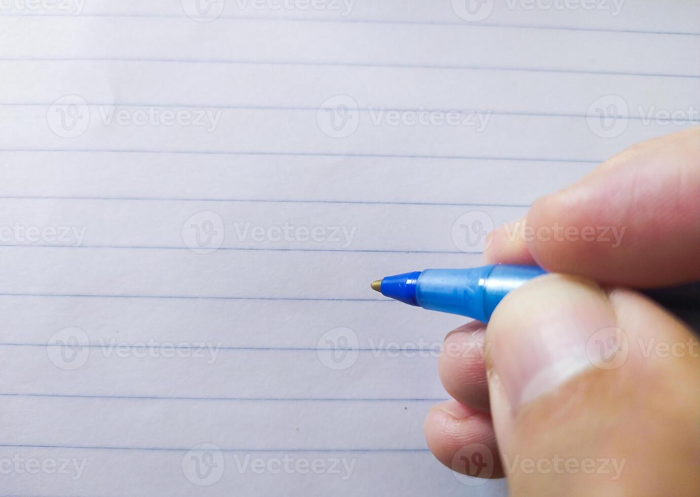 Closeup of a hand holding a blue pen above lined paper. Perfect for concepts of writing, education, notetaking, or backtoschool themes. photo