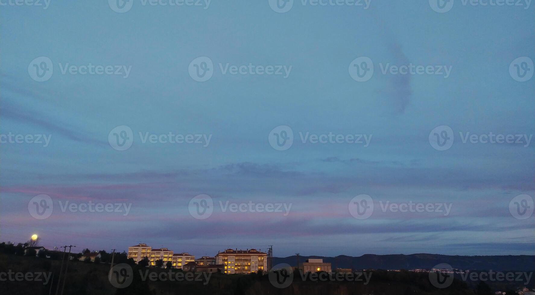 Serene twilight scene lowlight cityscape with residential buildings nestled against a hill, under a soft pastel sky. Perfect for tranquil, evening, or urban landscape themes. photo