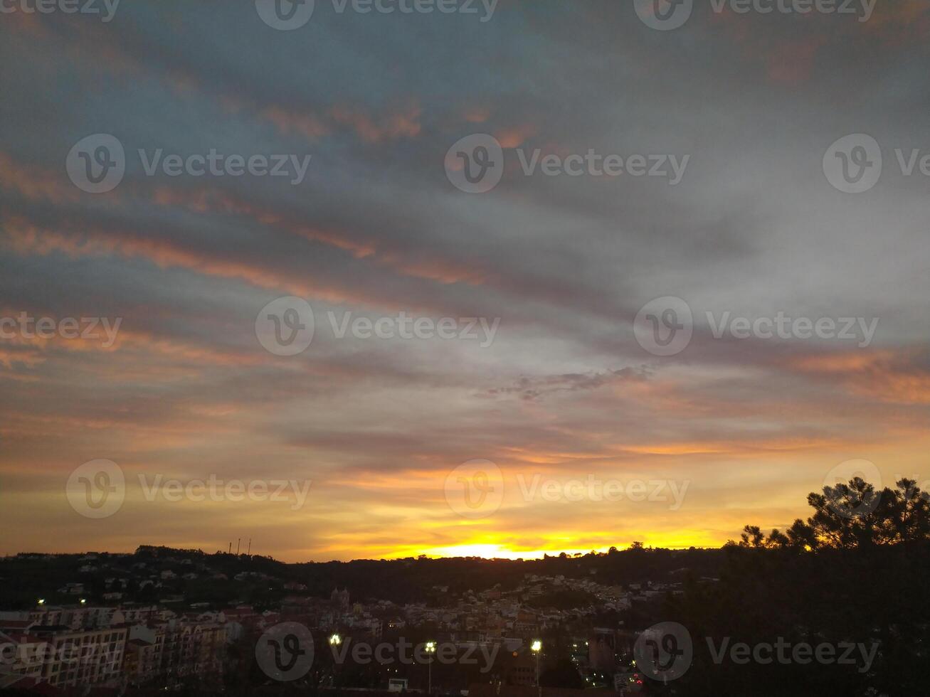 Stunning sunset over a cityscape. Warm golden hues paint the sky, contrasting beautifully with the dark silhouettes of buildings and trees. Ideal for travel, nature, or citythemed projects. photo