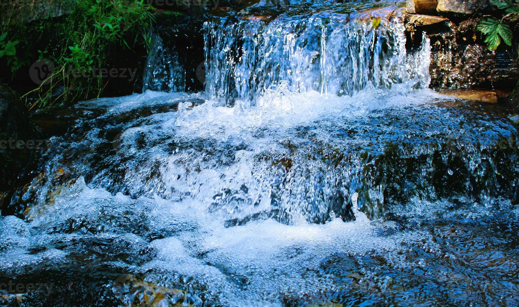 Pure mountain water foams in the streams of a small stepped waterfall photo