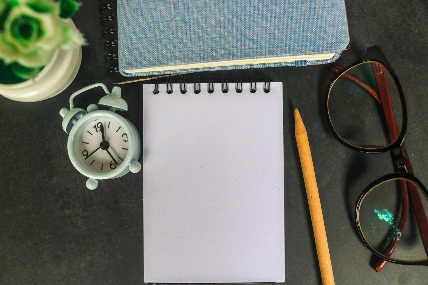 Blank notebook for text on gray office desk table with books, pen, plant, eyeglass, clock and other. Blank notebook page for input the text in the middle. Top view, flat lay. photo