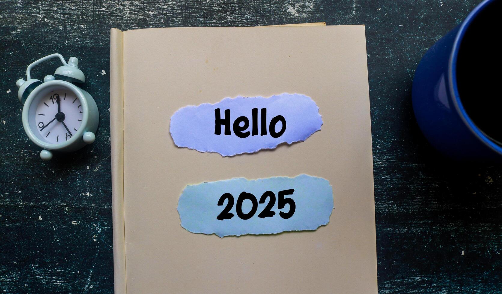 Hello 2025 text on notebook with alarm clock on wooden table. Welcoming the new year 2025 photo