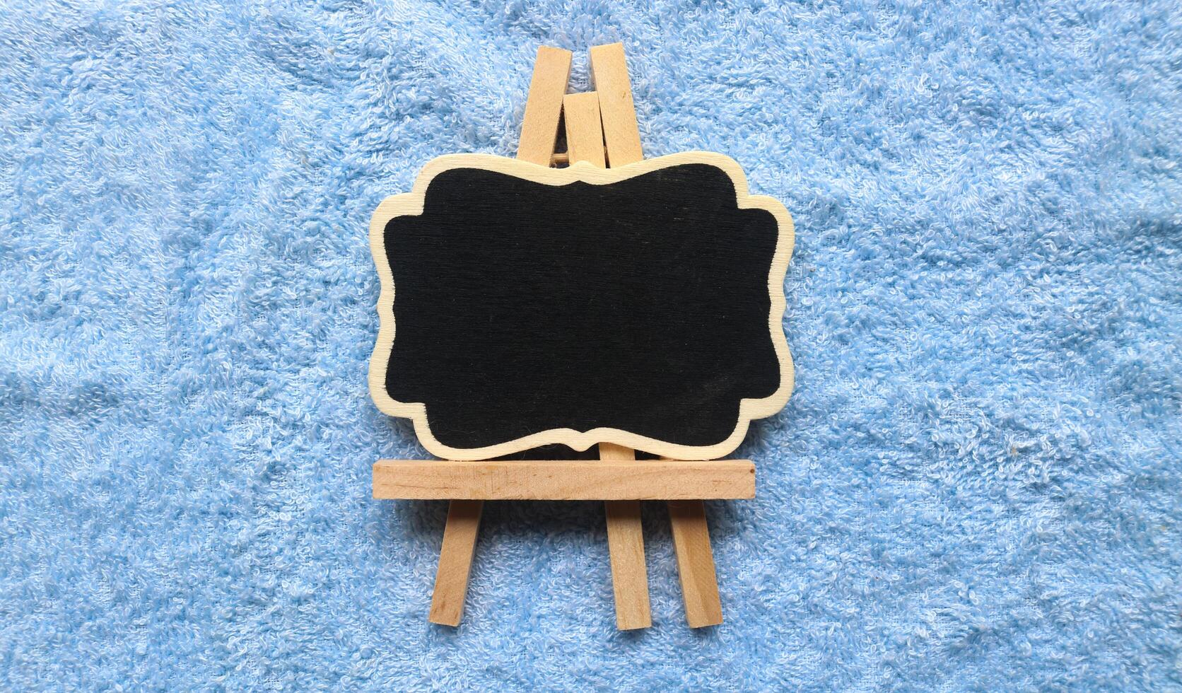Wooden easel mini blackboard with faded chalk surface, isolated on blue background. Blank space for text photo