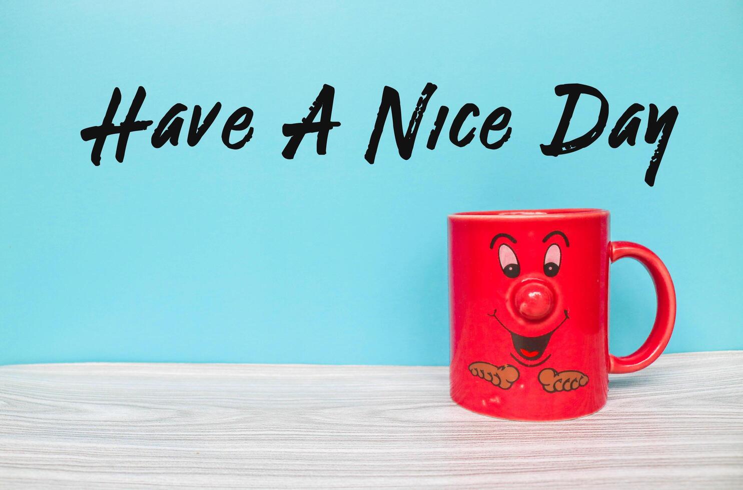 the words Have A Nice Day and red coffee cup with cartoon face emoji isolated with blue background photo