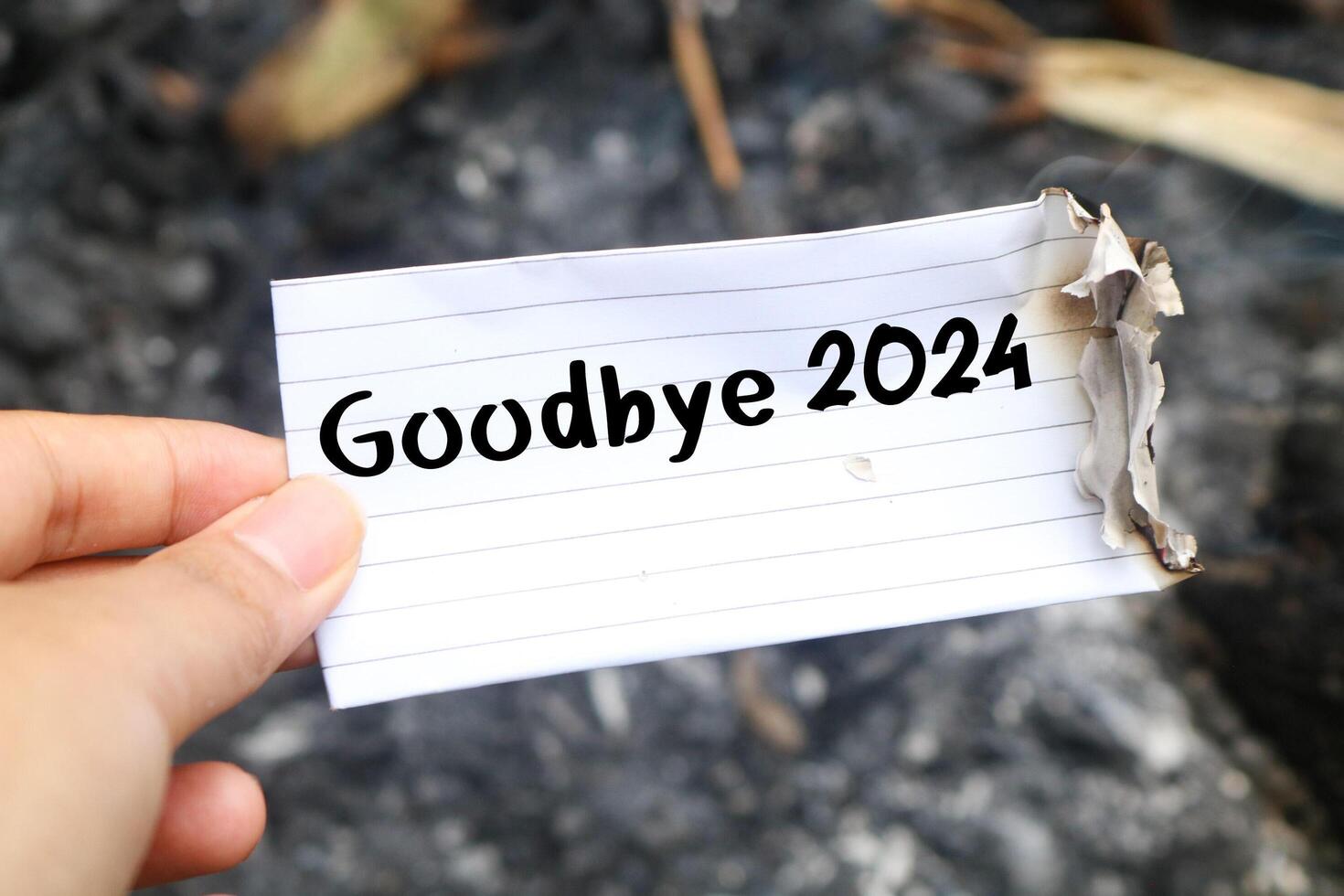 Hand holding burning paper on fire and pile of paper waste with Goodbye 2024 written on it. new life and new year 2025 concept. 2024 paper is burning, say goodbye to 2024 photo