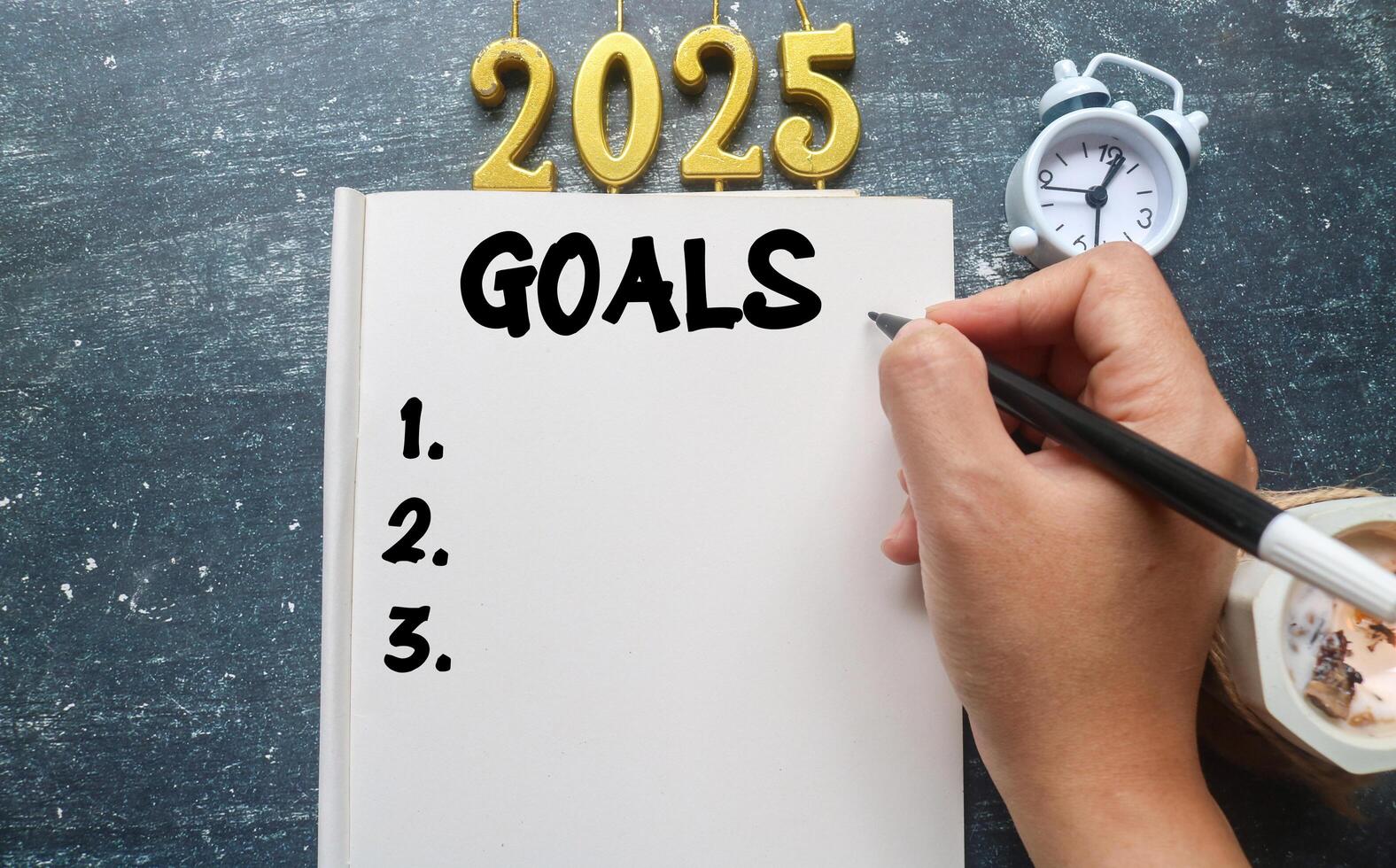 A person writes 2025 Goals in a notebook surrounded by aromatherapy candles and a clock. Planning to do list for 2025, life goals for 2025 photo