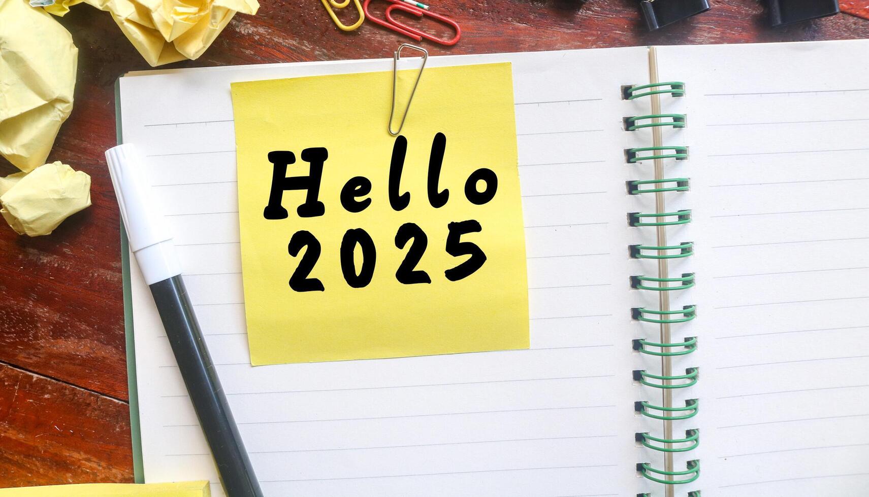 Yellow sticky note with Hello 2025 written on a notebook with stationery. Welcoming the new year 2025 concept photo