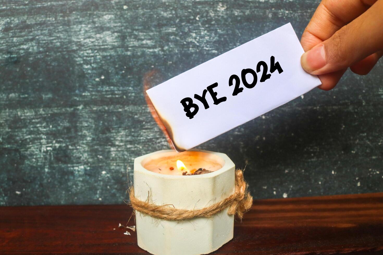 Hand holding a half-burnt note with Bye 2024 written on it on the candle. Burn the past 2024. Say goodbye to 2024. photo