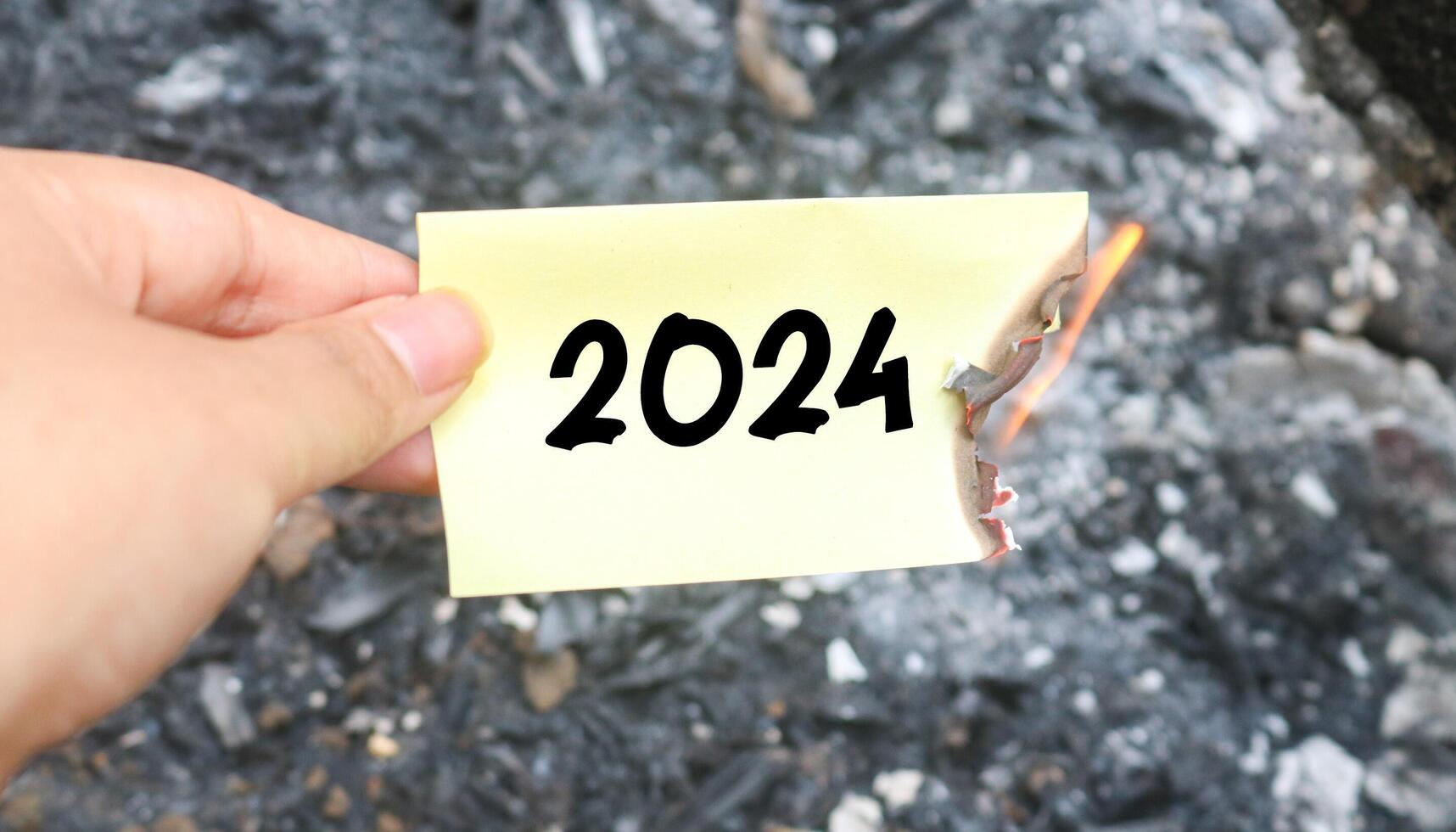 Hand holding burning paper on fire and pile of paper waste with 2024 written on it. new life and new year 2025 concept. 2024 paper is burning, say goodbye to 2024 photo