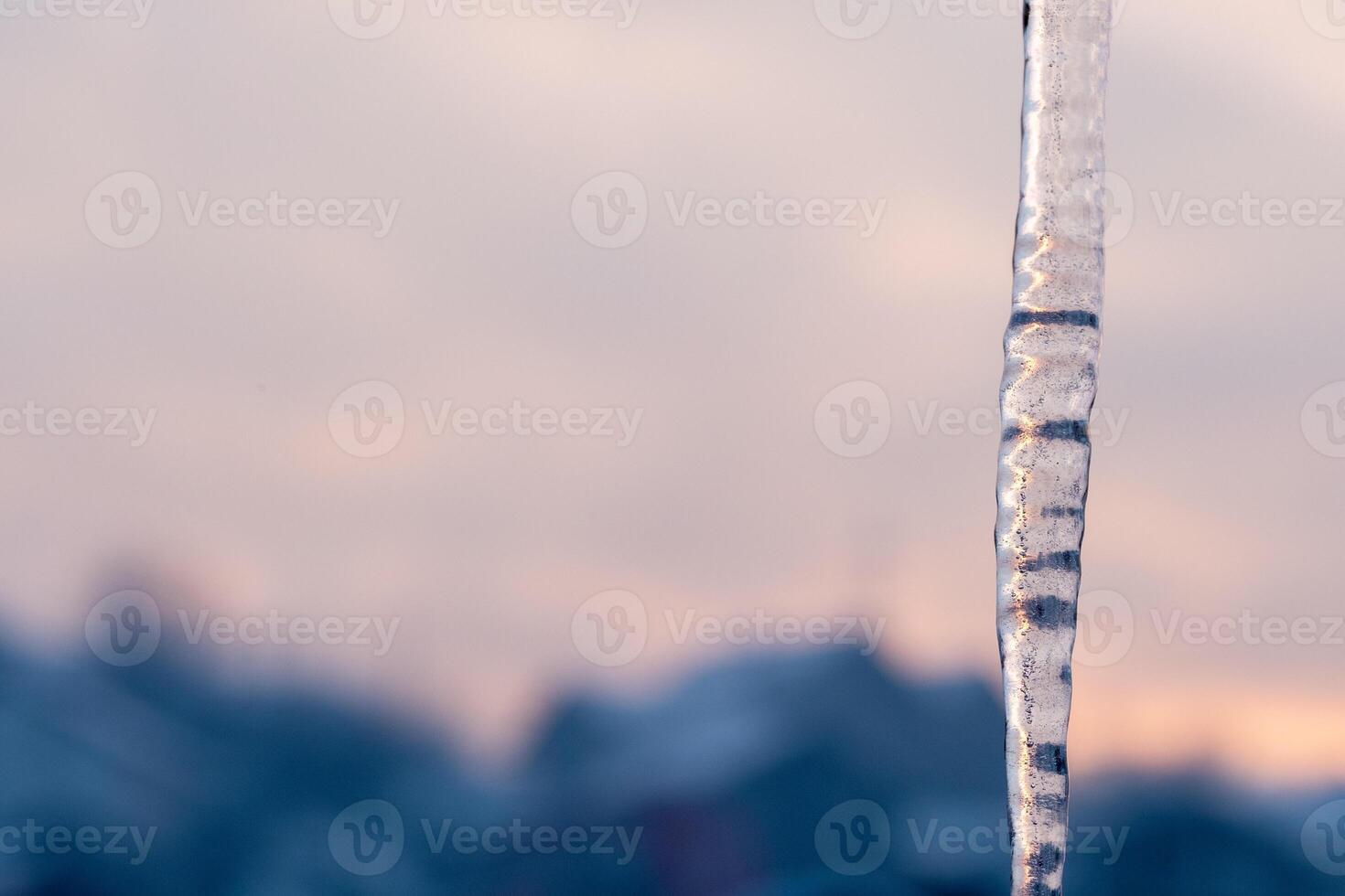 Close up of an icicle against a soft blurred sunset sky photo