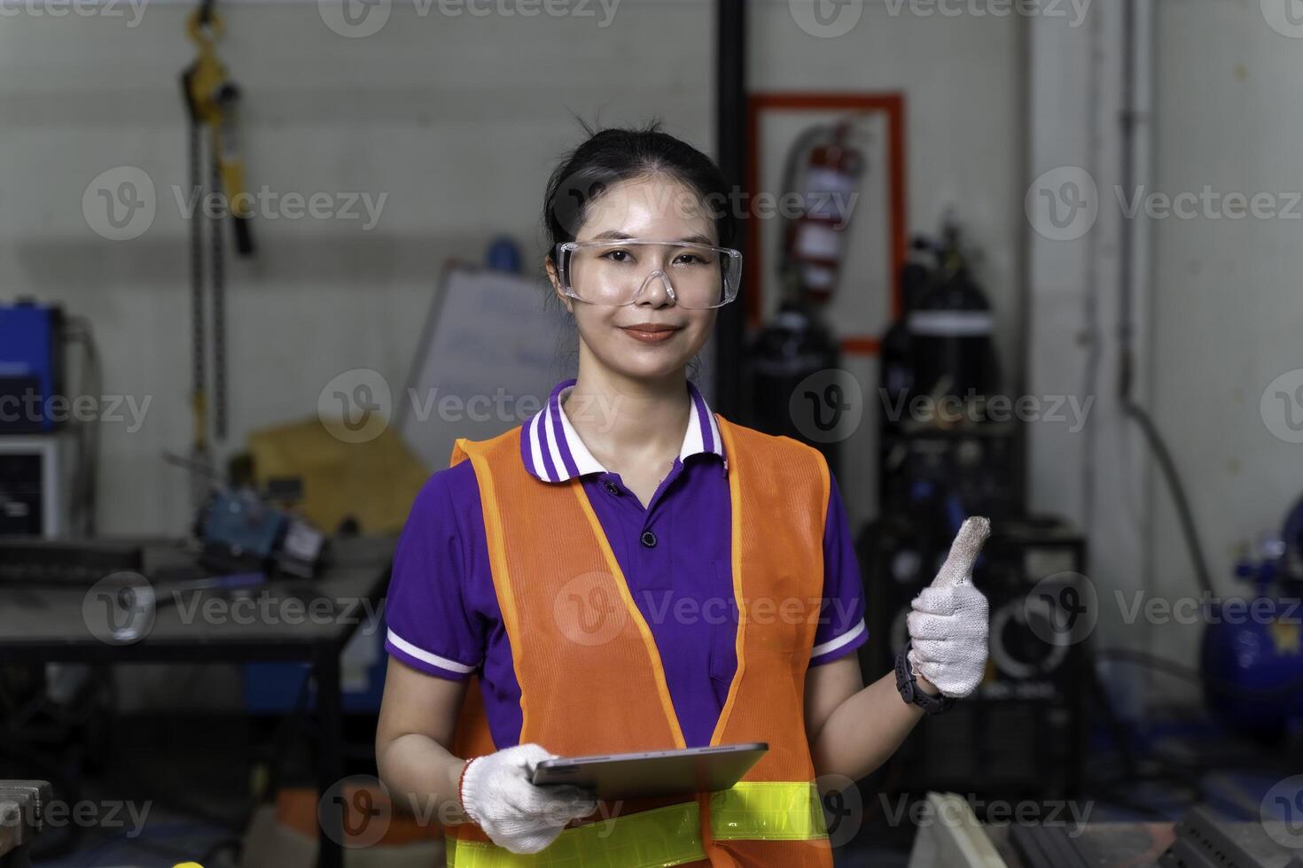 Construction worker, Asian woman engineer holding a tablet portrait of cheerful happy and thumbs up at industrial workshop. photo