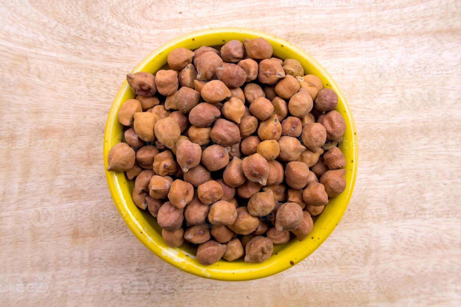 Flat Lay of Black or Brown Chickpeas in a Yellow Bowl on Neutral Wooden Background photo