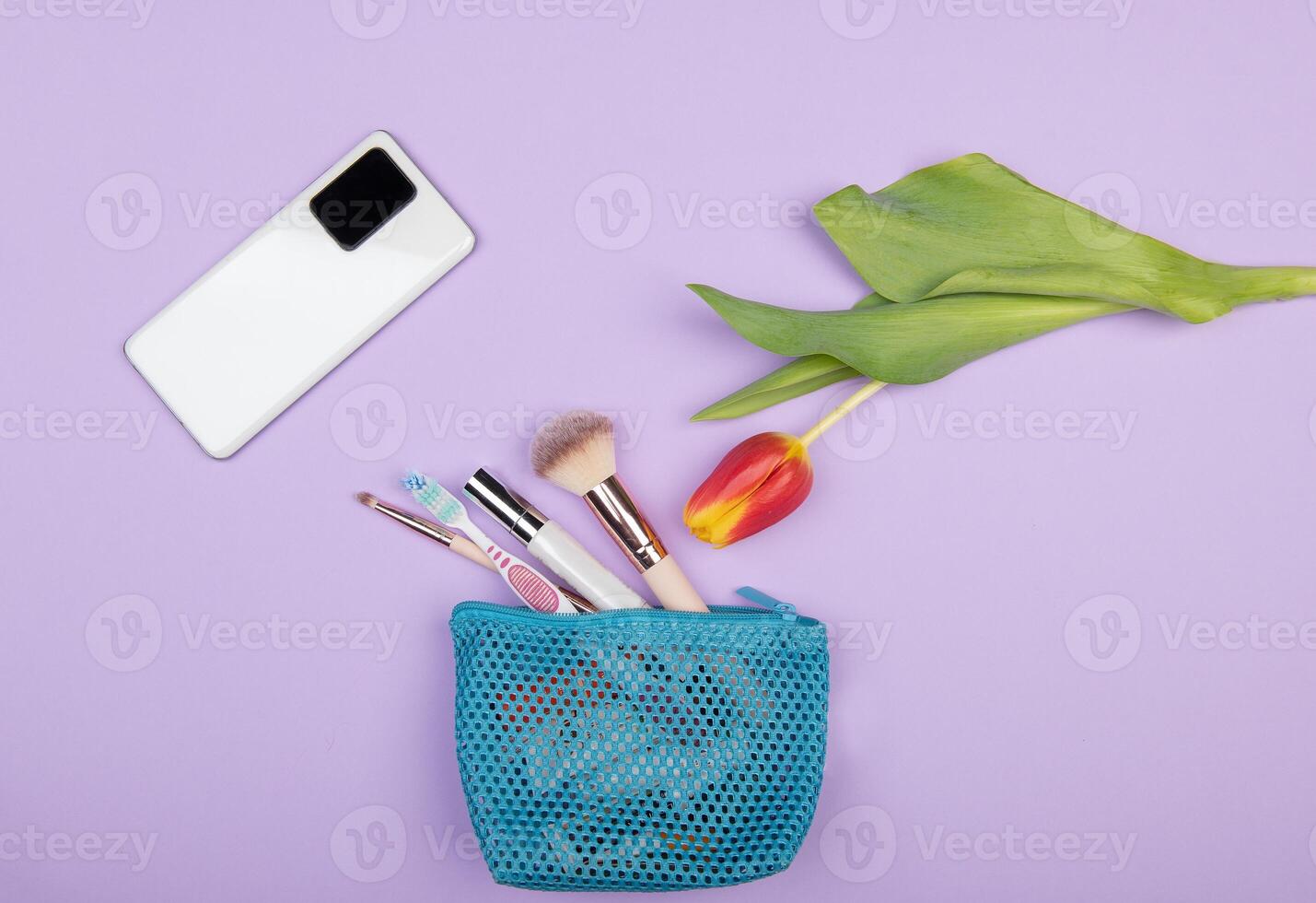 Travel flat lay with white smartphone, yellow tulip and makeup brushes on pastel photo