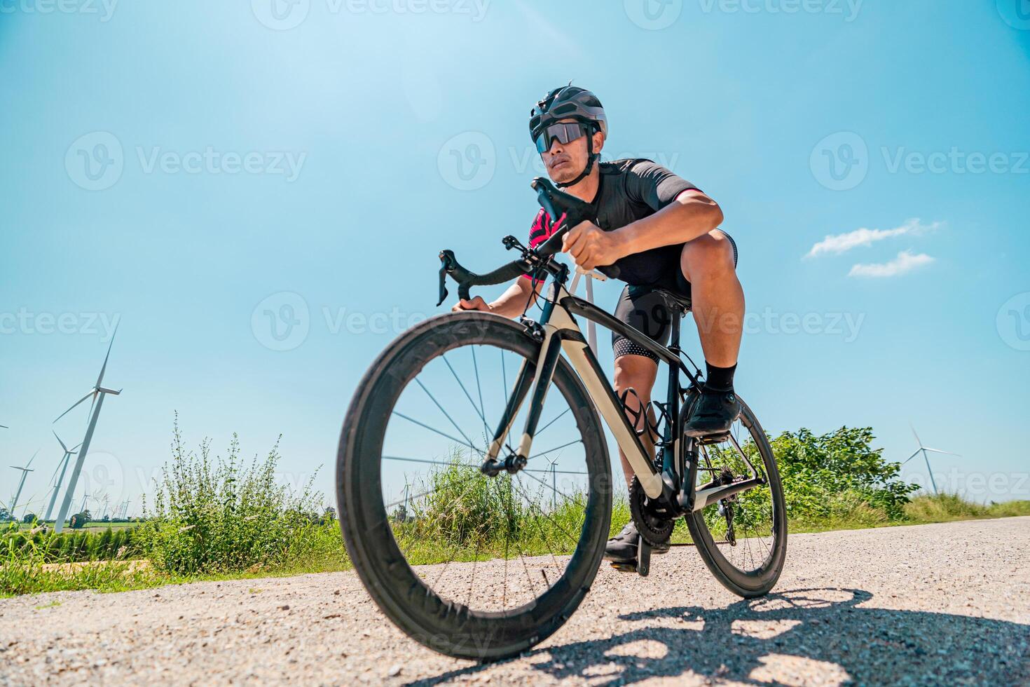 Cyclist riding on a sunny day near wind turbines on a scenic road surrounded by greenery photo