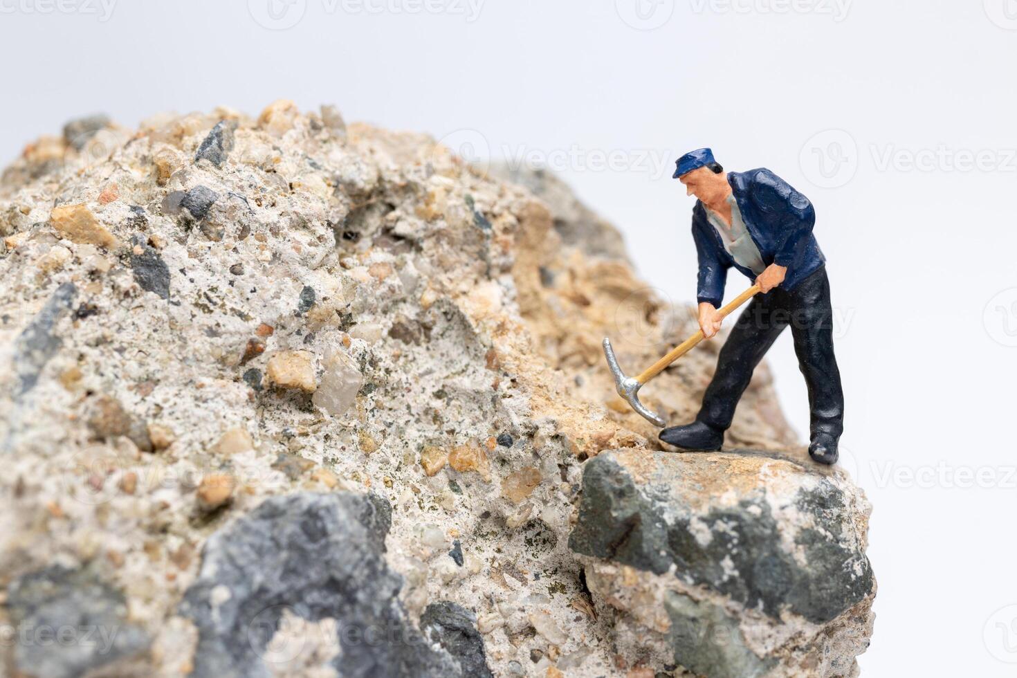 Miniature worker using a pickaxe to chip away at a large rock photo